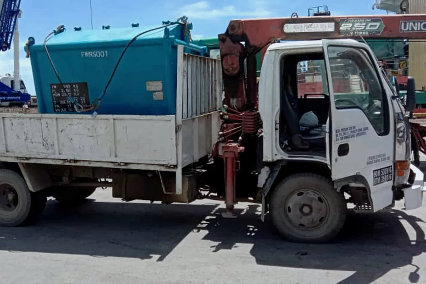 Teal waste skip rigged with slings beside a crane lorry
